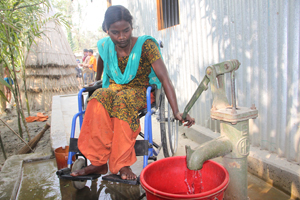 Woman in wheelchair pumps water by hand into container