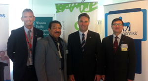 Four men in an office standing in front of program banners