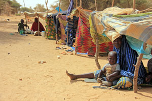 Children and women sit in small makeshift shelters at a temporary settlement site in the village of Mangaizé in Ouallam Department in Tillabéry Region