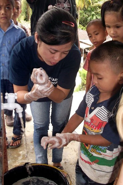 Woman showing children how to lather soap in their hands