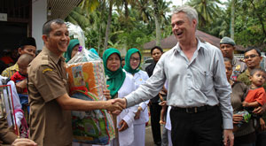 Mr Griffin and an Indonesian man smiling and shaking hands, with the Indonesian man holding a plastic bag full of toys