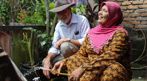 Mr Ramsay and an Indonesian woman smiling. The woman holds a hose from which fresh water flows.