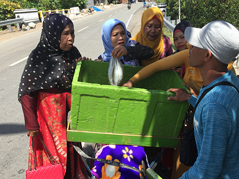 Group of women talking to man selling fish from box