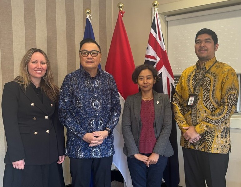 Four people standing in front of the NSW, Indonesian and Australian flags inside a room in the Consulate-General of the Republic of Indonesia (NSW).