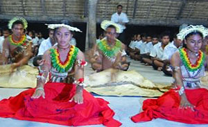 Photo of young people in traditional dress doing dance moves while seated on the ground