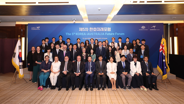A formal photo of a large group of people sitting and standing in rows in front of a large blue sign that reads The 5th Korea-Australia Future Forum in English and Korean. 