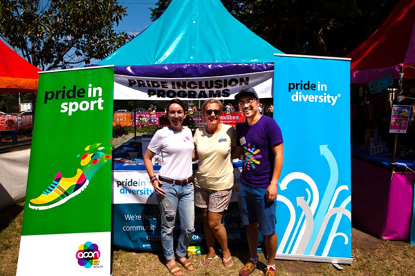 Three people at a fair stall with pride in diversity and pride in sport banners