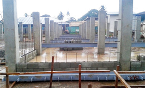 Wall of concrete blocks partially constructed, with frame laying on top waiting to be erected.