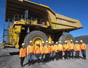 Visiting xx standing in front of and dwarfed by a massive yellow mining truck