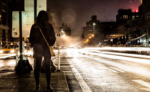 women standing on a busy street watching the traffic at night time