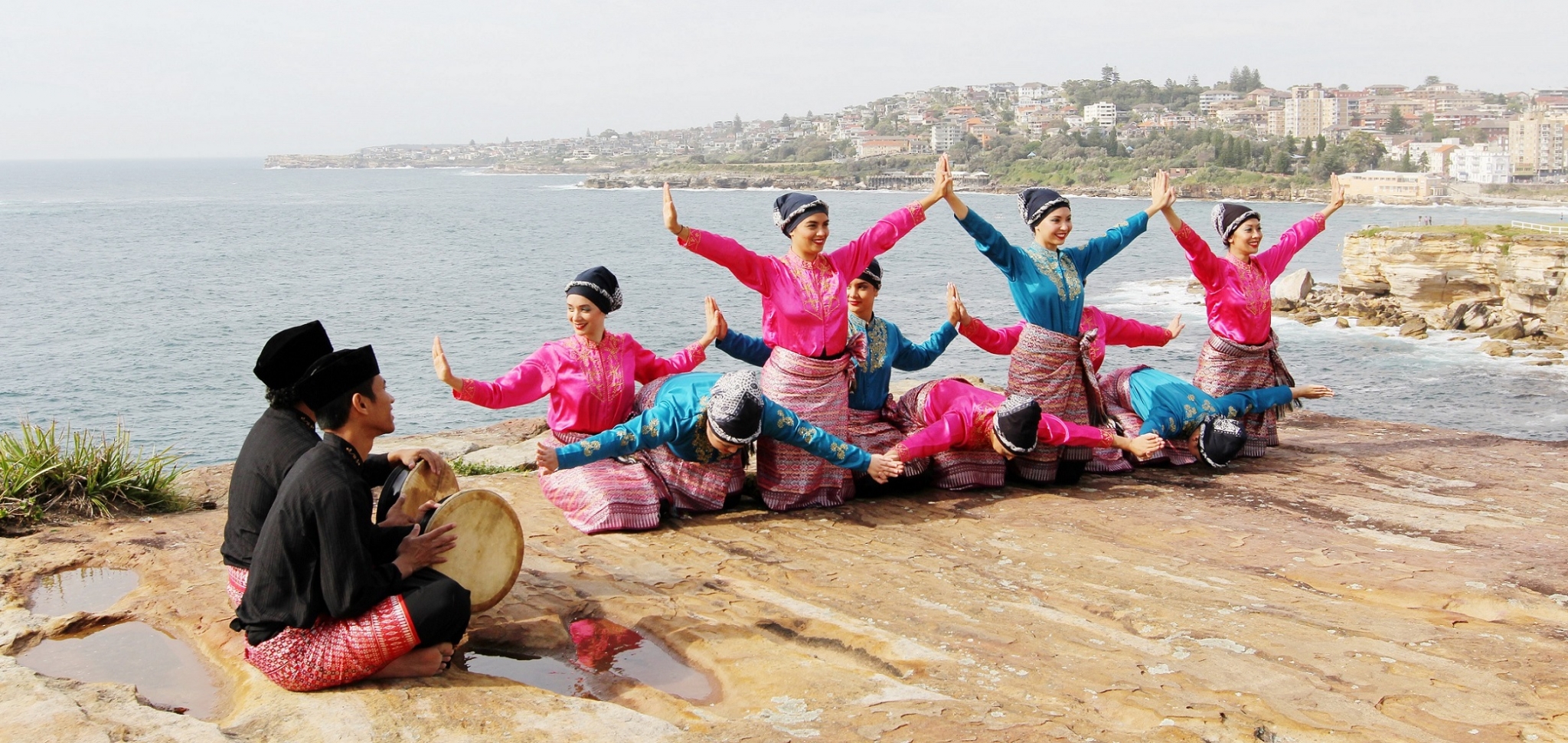 Group of dancers dressed in Indonesian traditional dress pose on cliffs with ocean in background