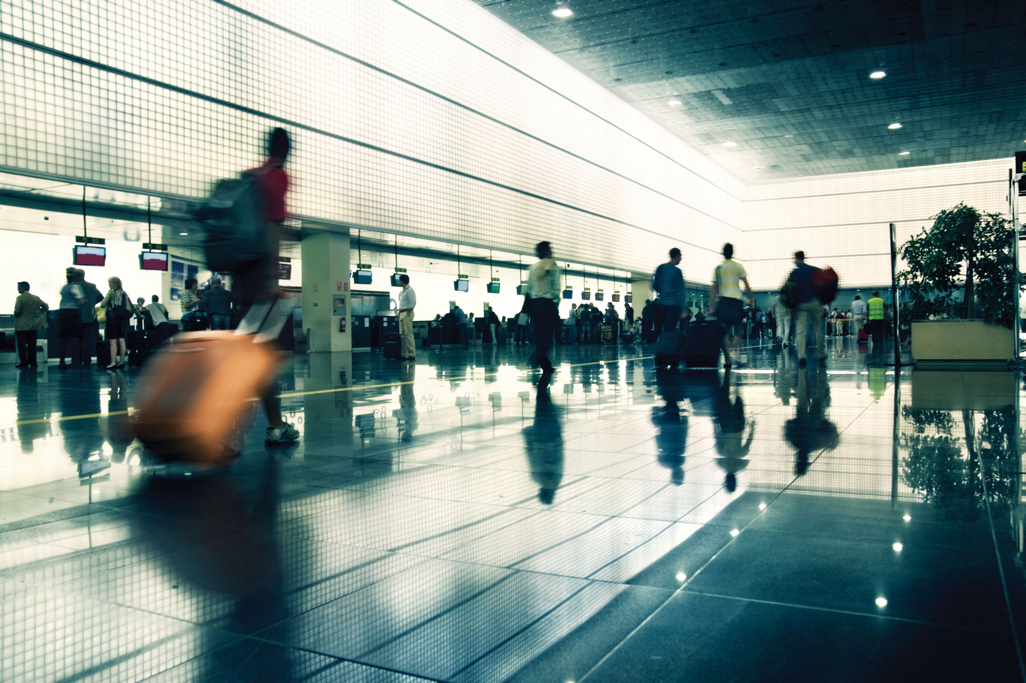 Airport departure hall, with several unidentifiable people pushing luggage trolleys and waiting in lounge areas
