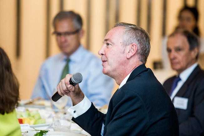 Guy speaks holding a microphone with people blurred in the background