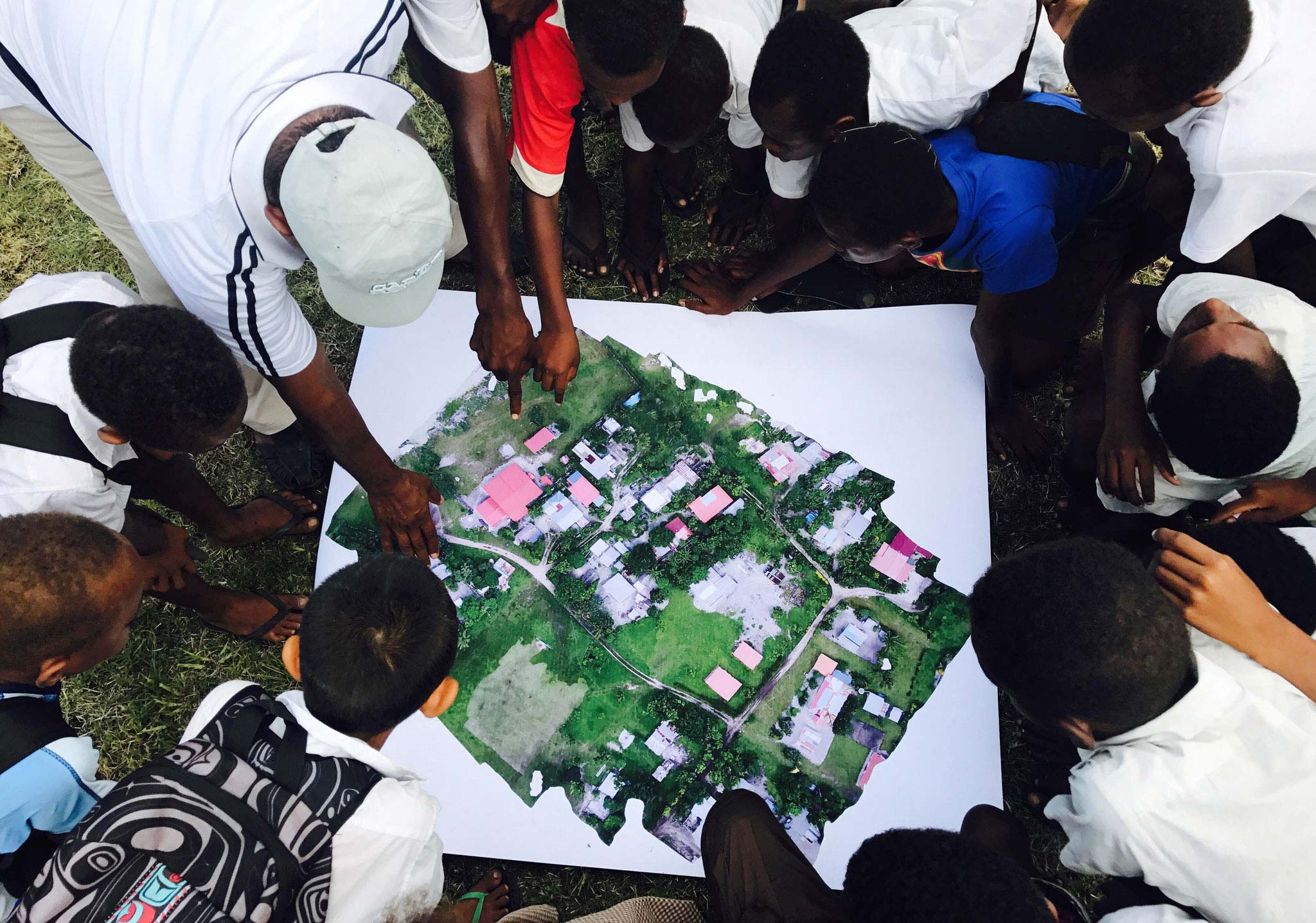Bird's-eye-view of a crowd looking and pointing at aerial images of a small village