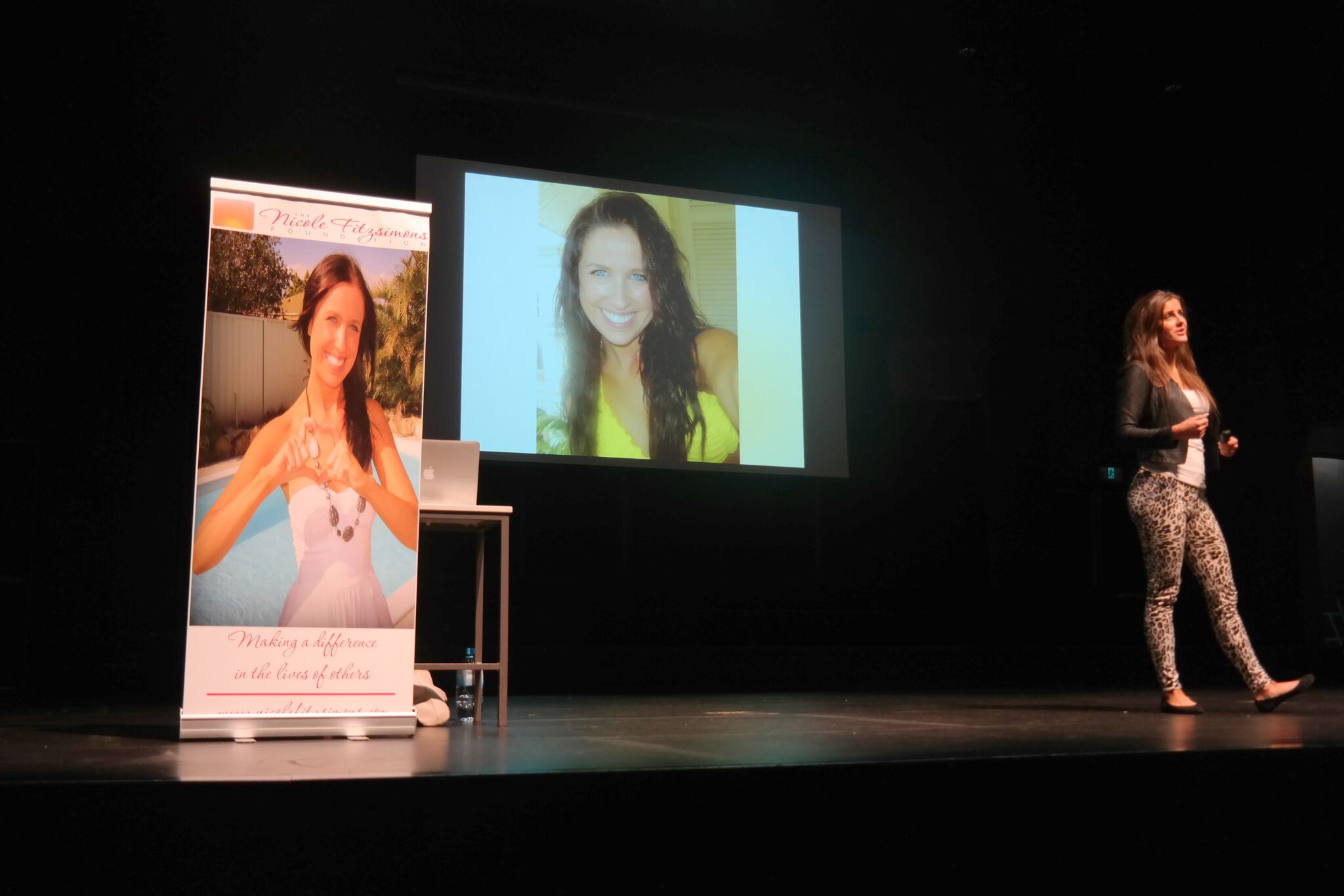 Kate Fitzsimons presents on a darkened stage with photos of her sister, Nicole, behind her