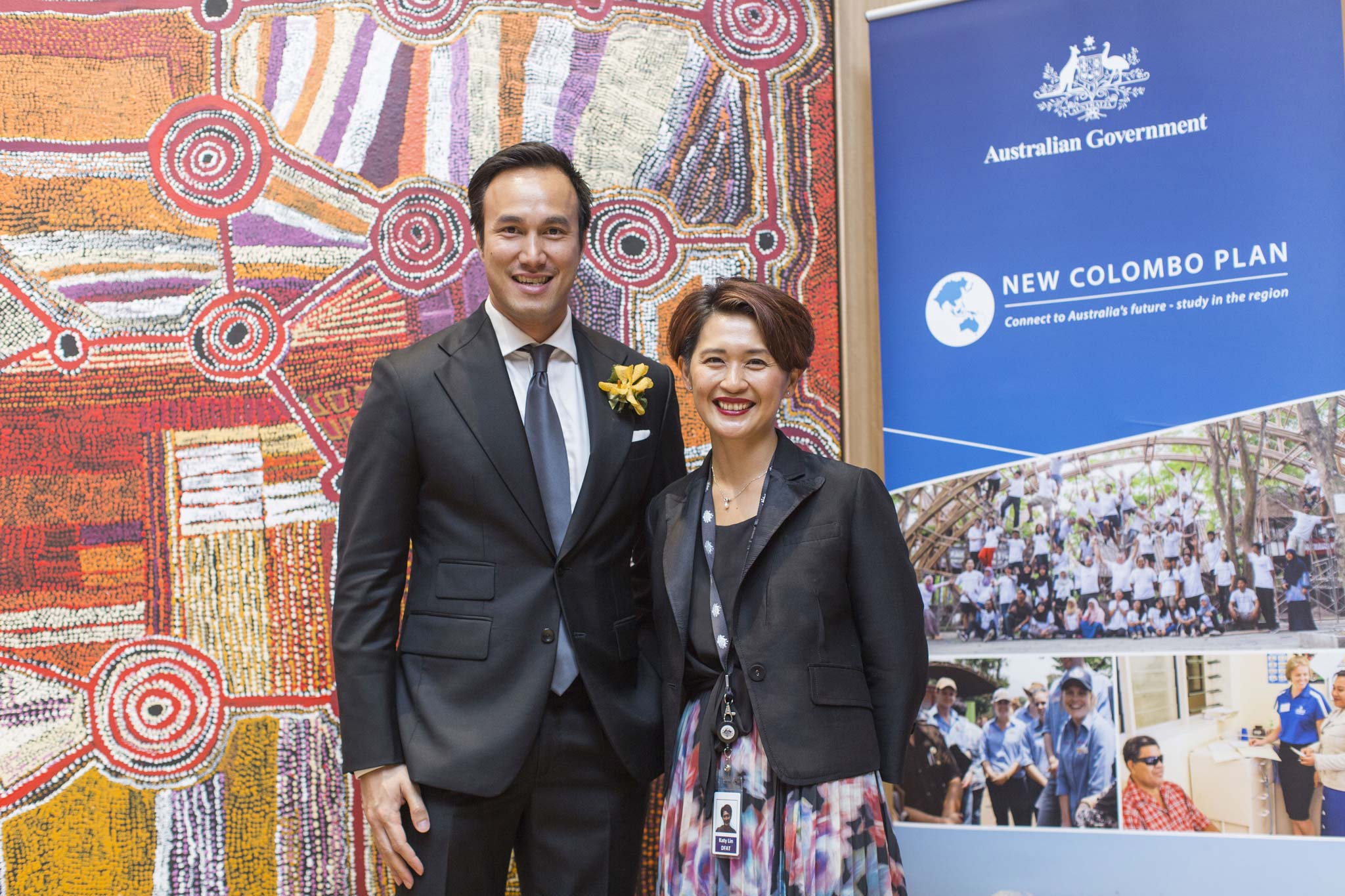 Katy Lin standing with a colleague in front of an Indigenous painting and a New Colombo Plan banner