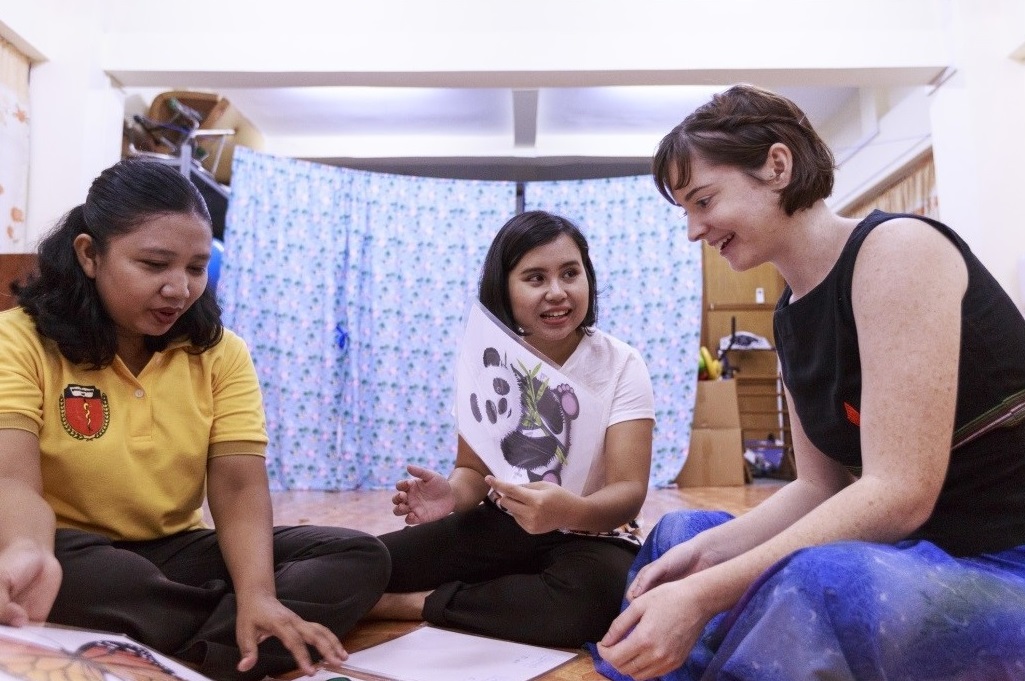 Krissy Wilhelmsen in conversation with two female colleagues in a medical room; woman in centre holding a drawing of a panda.