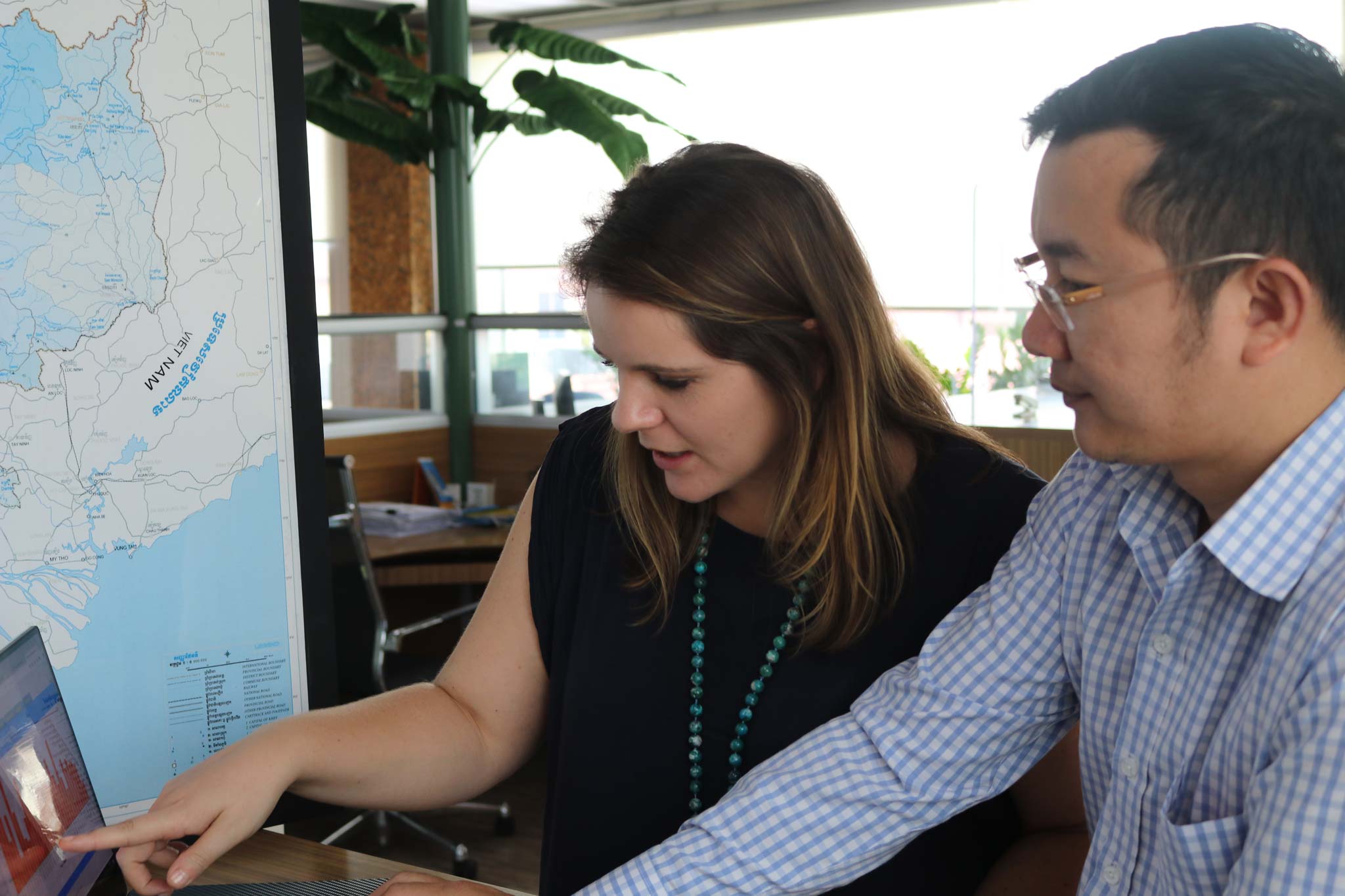 Stephanie Wheeler with a male colleague seated in an office looking towards a computer screen, map in background