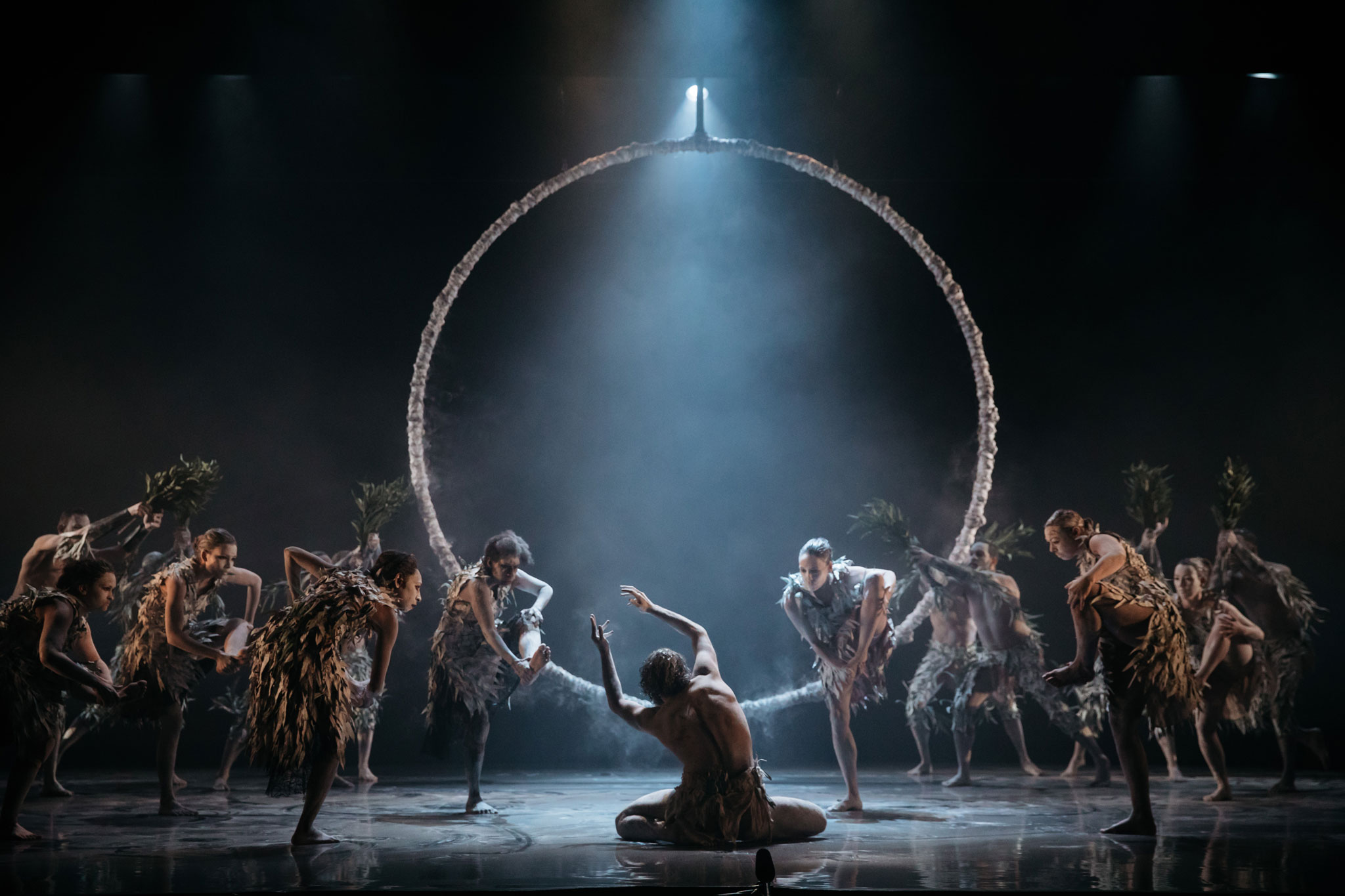 Large group of Bangarra (Indigenous dance group) dancers performing on stage, with large ring prop at centre
