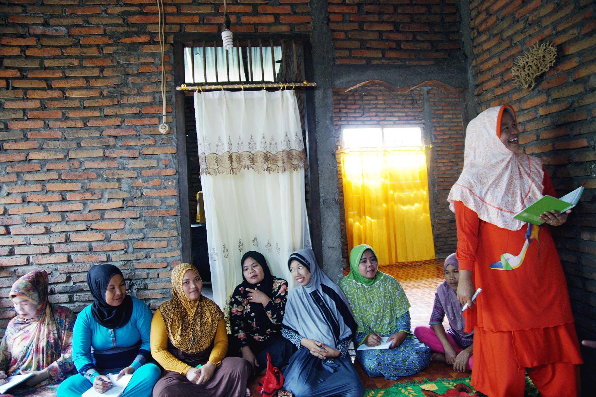 Syamsiah, standing, in front of a group of seven seated women in a classroom setting