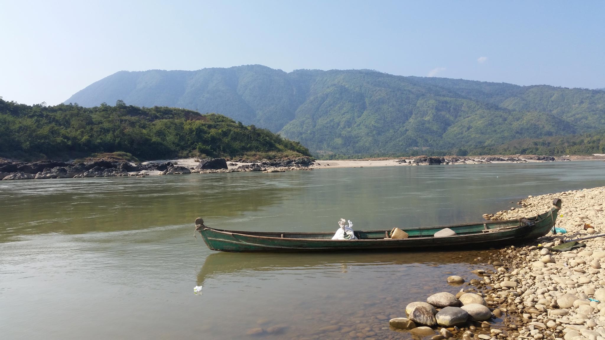 Empty low boat on flat river in front of green hills