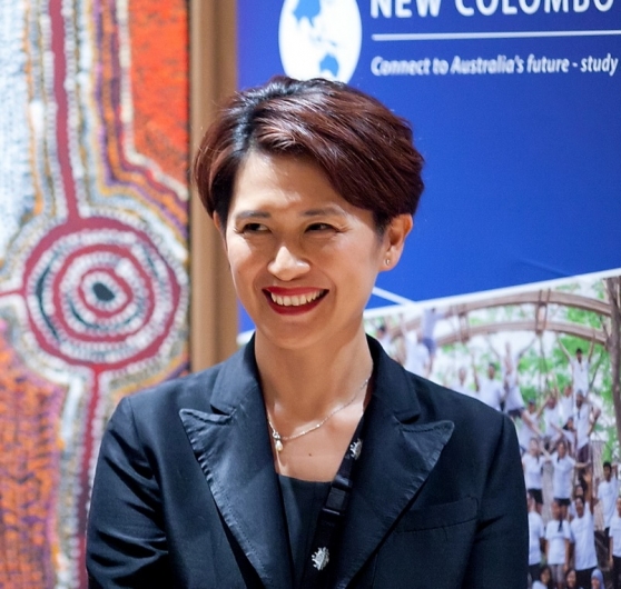 Close up of Katy Lin, with detail of an Indigenous painting and a blue banner behind her