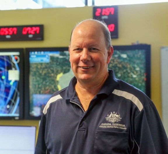 Peter Welch standing in front of technical equipment, including a screen with map of Australia to left