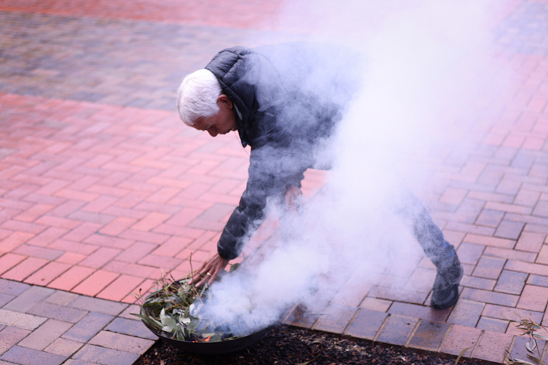A man adds leaves to a small fire during a smoking ceremony.