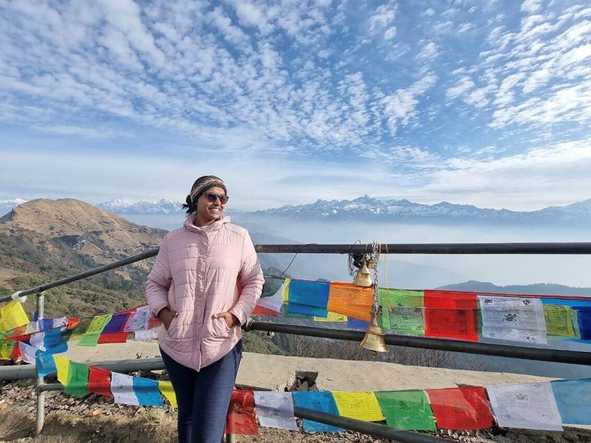 Harine leaning back on a railing, draped with flags up on top of a mountain