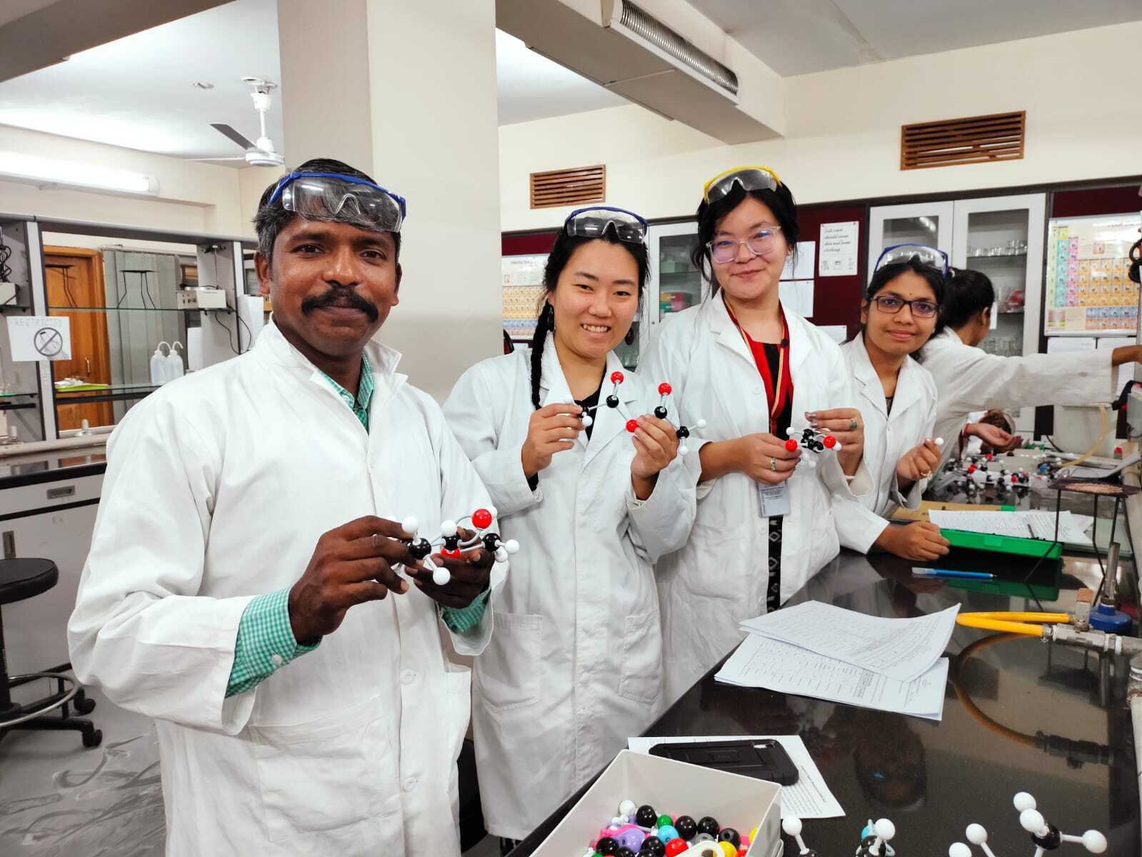 Jasmine in a white coat and goggles on head with three colleagues