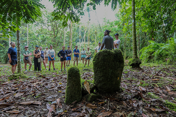 13 people standing in a semicircle talking to a local professional.