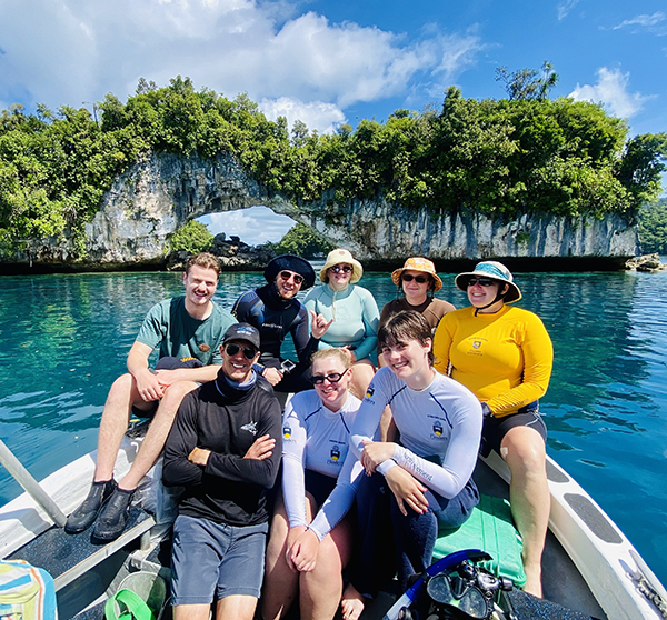8 students sitting in a boat on the ocean with island in the back ground