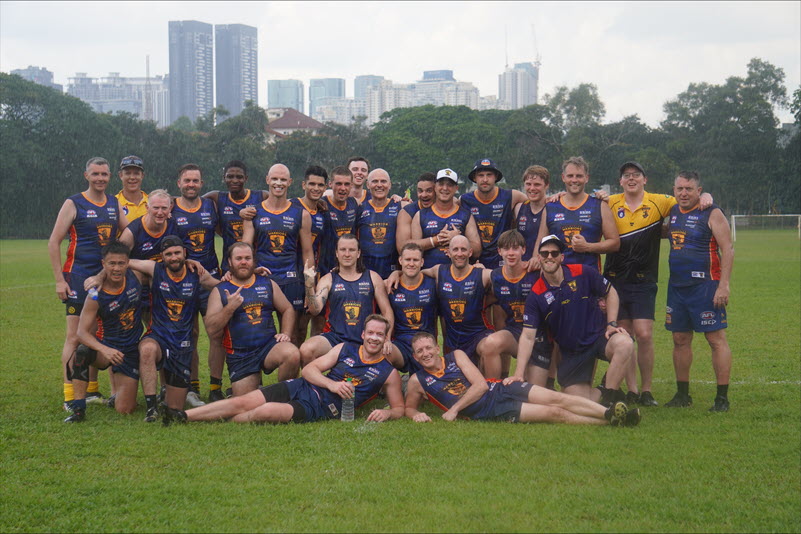 A team photo of AFL players in their sports uniforms posing in two rows. Ricky is standing in the back row, seventh from the left.