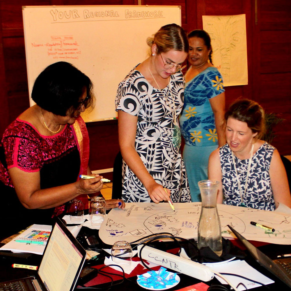 Photo of Soraya McGinley with representatives of the World Bank and the Pacific Community in discussion at a desk with several papers in front of them.