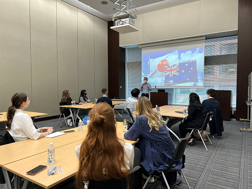 Students sitting around a table watching a presentation on a screen.