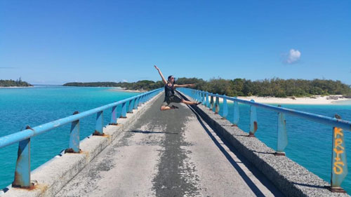 Ella performing a ballet move on a bridge with the island in the background.