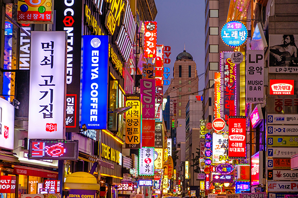 Street level photo of a busy Seoul market district with colourful Korean billboards. 