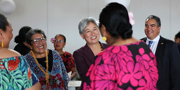 Group of people talking at an indoor event, with several wearing colourful patterned clothing and floral accessories.