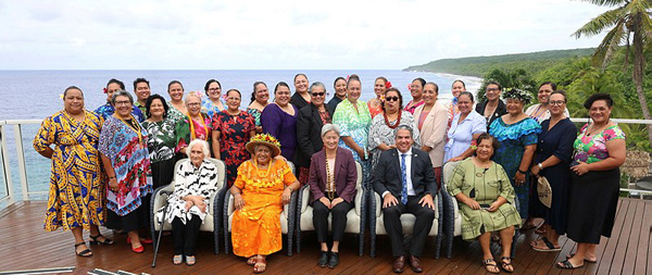 Group of people posing for a formal photograph outdoors, with the ocean and tropical landscape in the background.