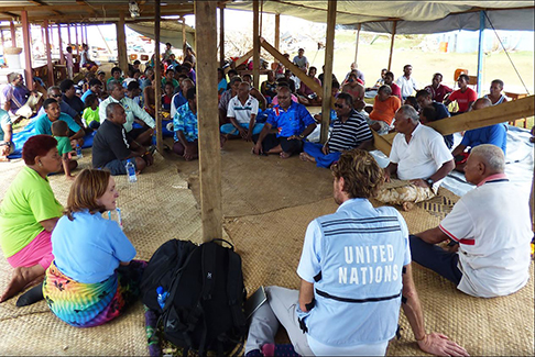 Large group of people sitting and talking, under outdoor shelter