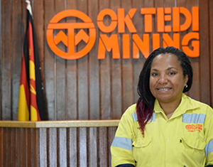 Mokica Koek standing in front of Ok Tedi Mining logo