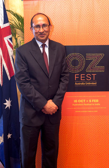 Peter Varghese standing next to an Australia Flag and a banner advertising Oz Fest.