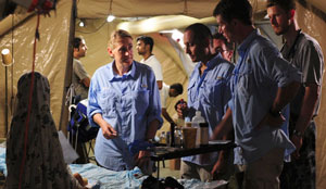 Photo of several men and women medical personnel grouped around a bed, with a baby and her mother