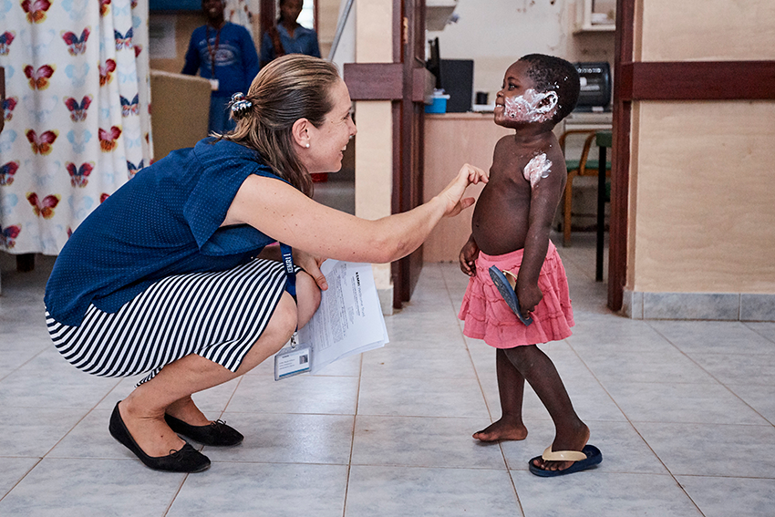 Dr Phoebe Williams bending down at eye level with, and reaching out to, a young patient