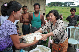 A woman hands another woman two bags of food, with men and children looking on