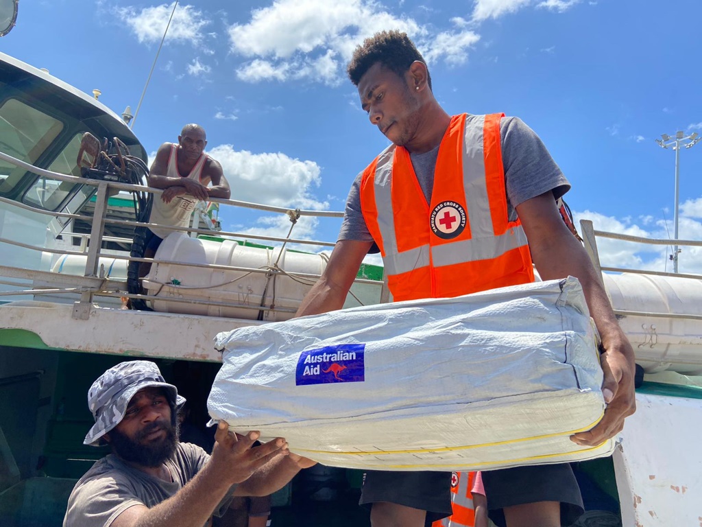 One man representing the Vanuatu Red Cross Society passes Australian Aid branded supplies to another man, to be distributed to those affected by the cyclone