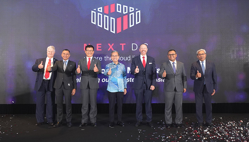 Seven men standing with their thumbs up in front of a NEXTDC promotional backdrop.