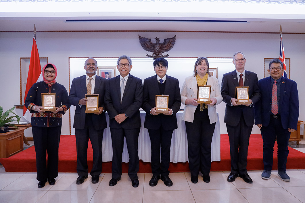 Seven people in a line, five of which are holding up small plaques.