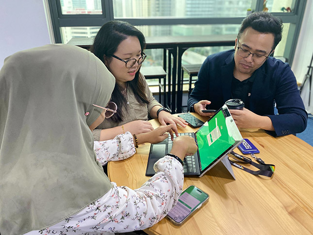 Three employees sitting around a desk working on one laptop.