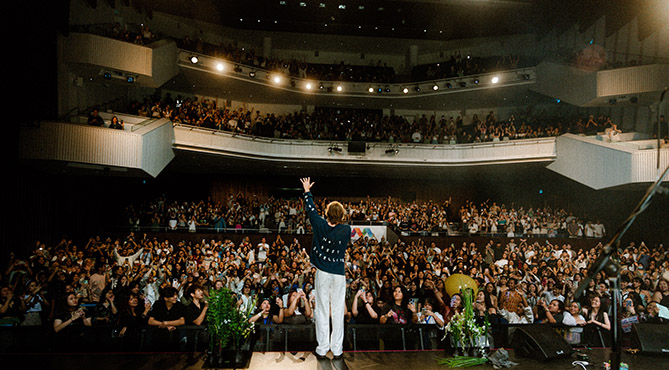 Male singer performing in front of a full theatre with his back turned to camera.